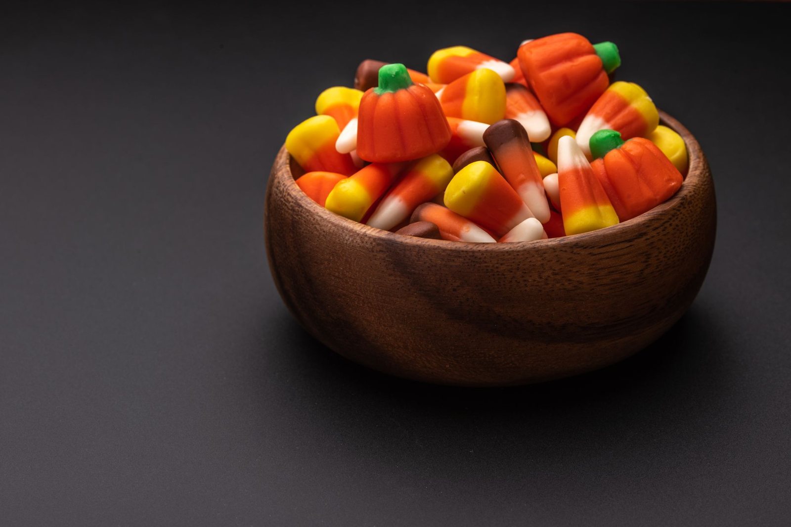 A wooden bowl full of candy corn on a dark table