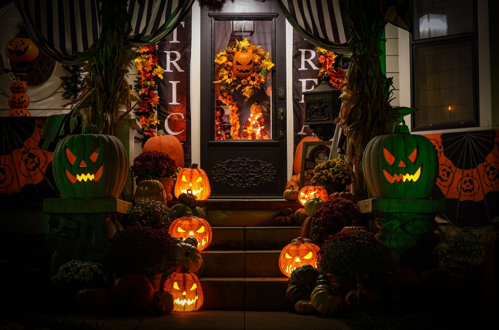 Uma varanda de casa decorada com abóboras acesas e crisântemos ao anoitecer