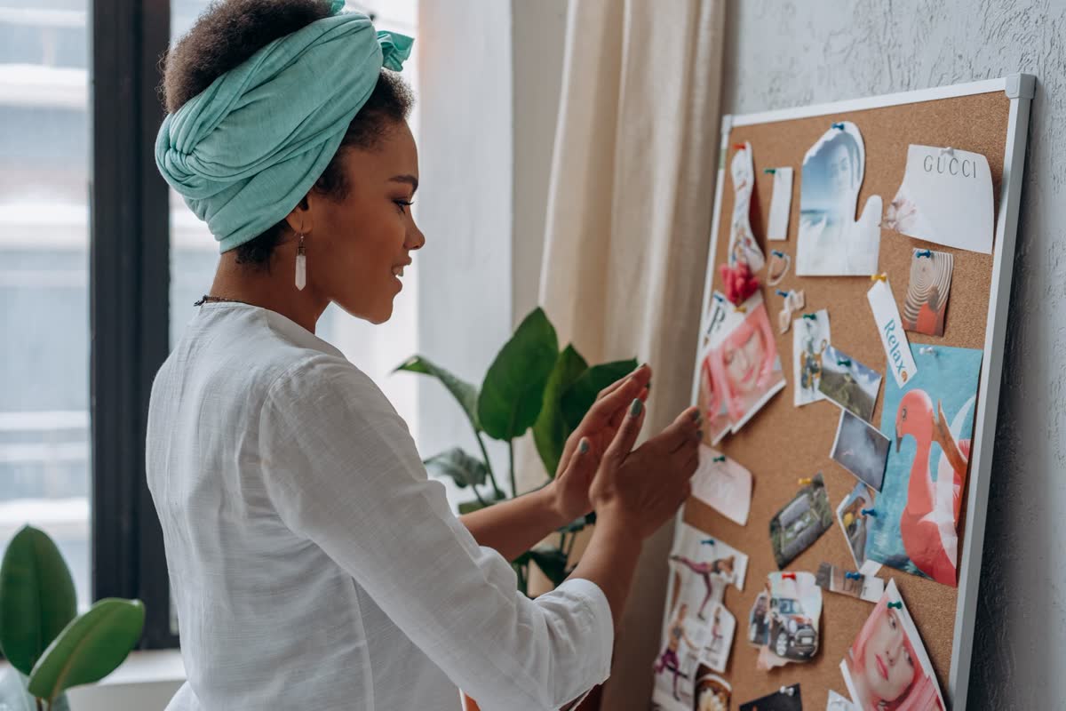 A person pinning notes and photos to a cork board on the wall