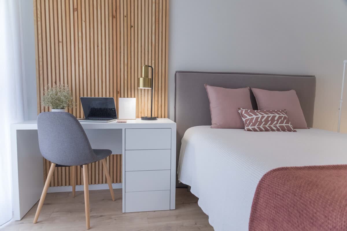 A compact white study desk with a chair against a wall in a bedroom